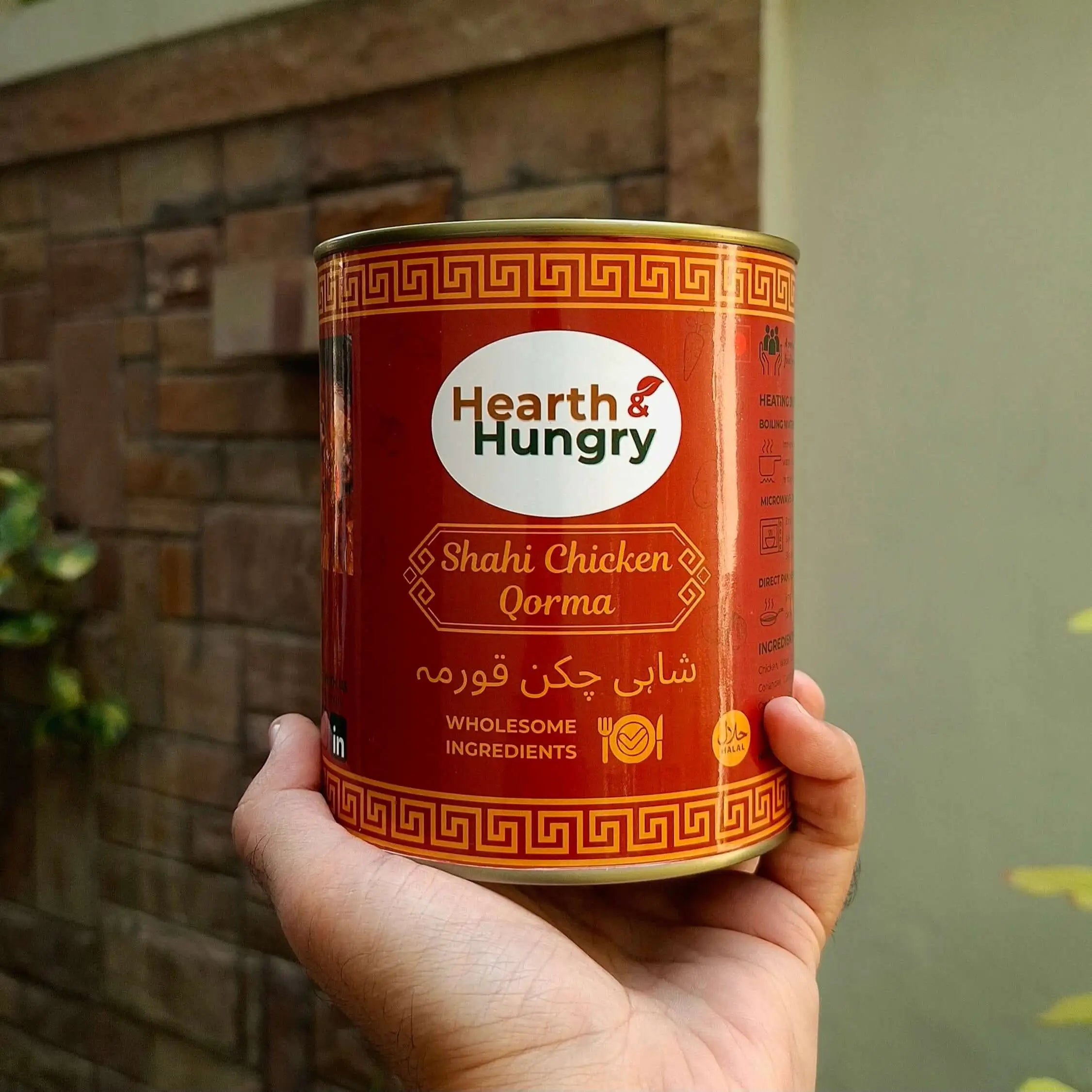 Holding a meal tin of Shahi Chicken Qorma against a wooden brick wall
